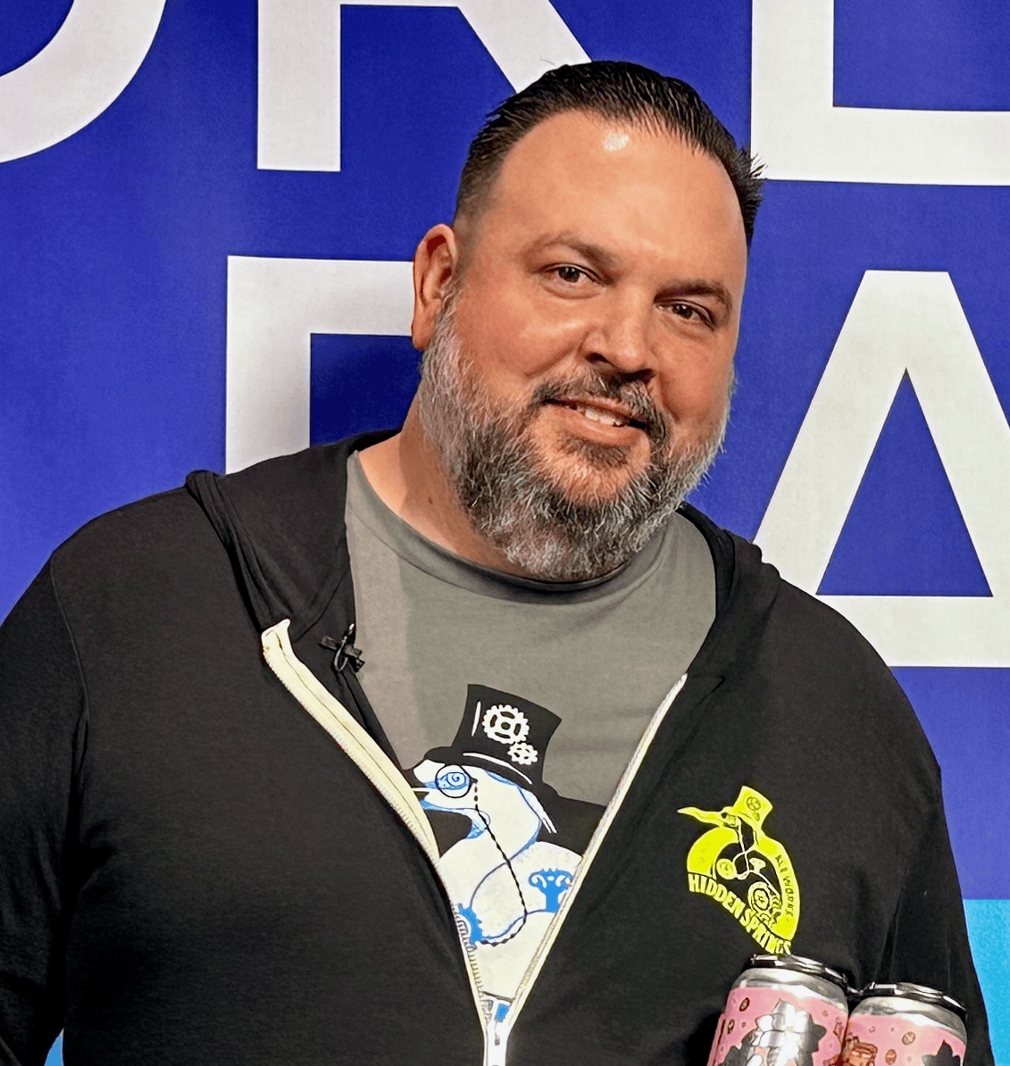 Josh Garman, founder and CEO of Hidden Springs Ale Works, wearing a black logo jacket and holding a can of Blush & Bashful Cru Cellars collaboration sour beer